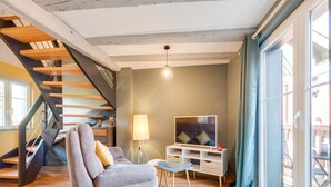 Una sala de estar con un sofá gris, un televisor, una lámpara y una escalera.