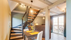 Un interior moderno con una escalera de madera, un comedor con mesa y sillas, y un balcón con mobiliario exterior.