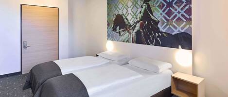 Habitación de hotel con dos camas, una puerta, una obra de arte colgada en la pared y una mesita de noche con lámpara.
