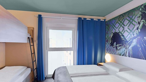 Een hotelkamer met stapelbedden, een raam met gordijnen, een muur met een grafische afbeelding en een vloerbedekking.