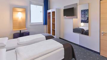 Une chambre d’hôtel avec deux lits, une télévision, un miroir, une fenêtre avec des rideaux et une armoire.
