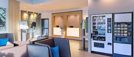 Un vestíbulo de hotel moderno con zonas de estar, un mostrador de recepción y máquinas expendedoras.