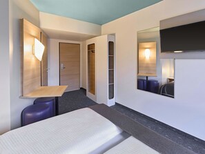 Una habitación de hotel moderna con una cama, un pequeño escritorio, un espejo y un armario.