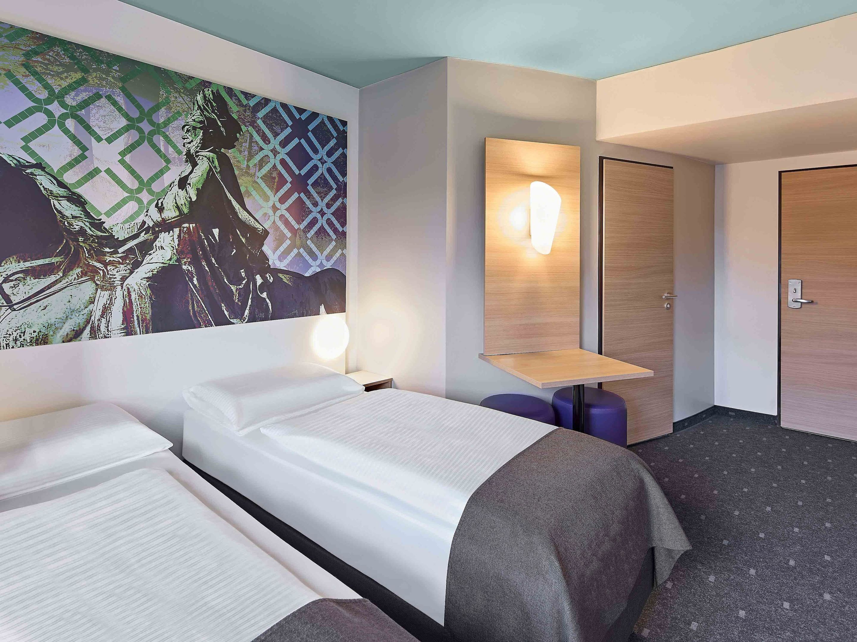 Una habitación de hotel con dos camas, una lámpara de pared, una mesita y una puerta.
