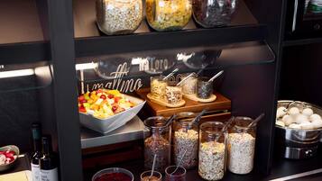 A buffet area with various food items, including a bowl of fruit salad, jars of nuts and seeds, and a bowl of red fruit compote.