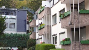 Un edificio residencial de varios pisos con balcones, una escalera y un coche estacionado en la calle.