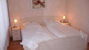 Una cama bien hecha con sábanas blancas, dos mesitas de noche con lámparas, y un cuadro en la pared.
