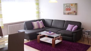 Una sala moderna con un sofá gris oscuro, una mesa de centro de vidrio y un tapete morado.