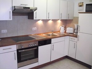 A modern kitchen with white cabinets, a stainless steel range hood, a built-in oven, a dishwasher, and a double sink.