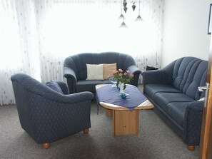 Ein Wohnzimmer mit zwei Sesseln, einem Sofa, einem Holztisch und einer Vase mit Blumen.