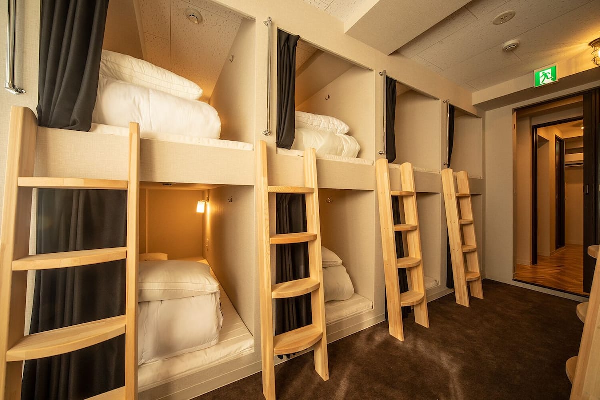 A hotel room with bunk beds, wooden ladders, and a visible exit sign.