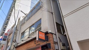A building corner with a 'Naruto' sign, a brick facade, and a window with a metal frame. - The Terrace Hostel Shinbashi (Tokyo)