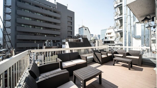 A rooftop terrace with wicker furniture, a white railing, and a view of surrounding buildings. - The Terrace Hostel Shinbashi (Tokyo)