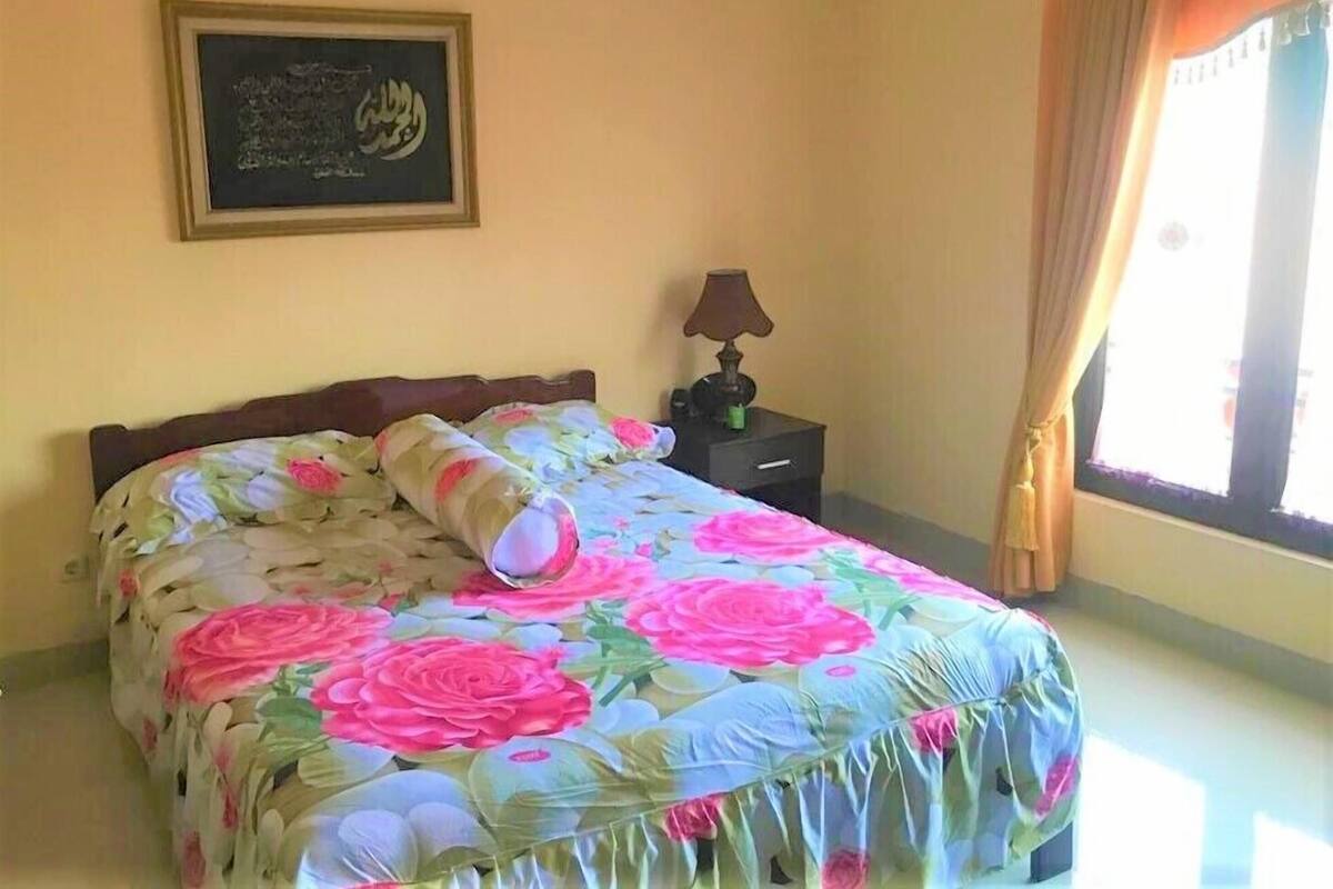 A bedroom with a bed, a nightstand, a lamp, a framed picture on the wall, and a window with curtains.