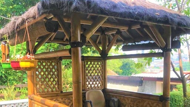 A bamboo structure with a thatched roof, a cushioned bench, and potted plants. - Poetri Guest House Syariah (Bogor)