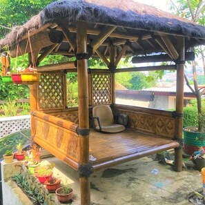 A bamboo structure with a thatched roof, a cushioned bench, and potted plants. - Poetri Guest House Syariah (Bogor)