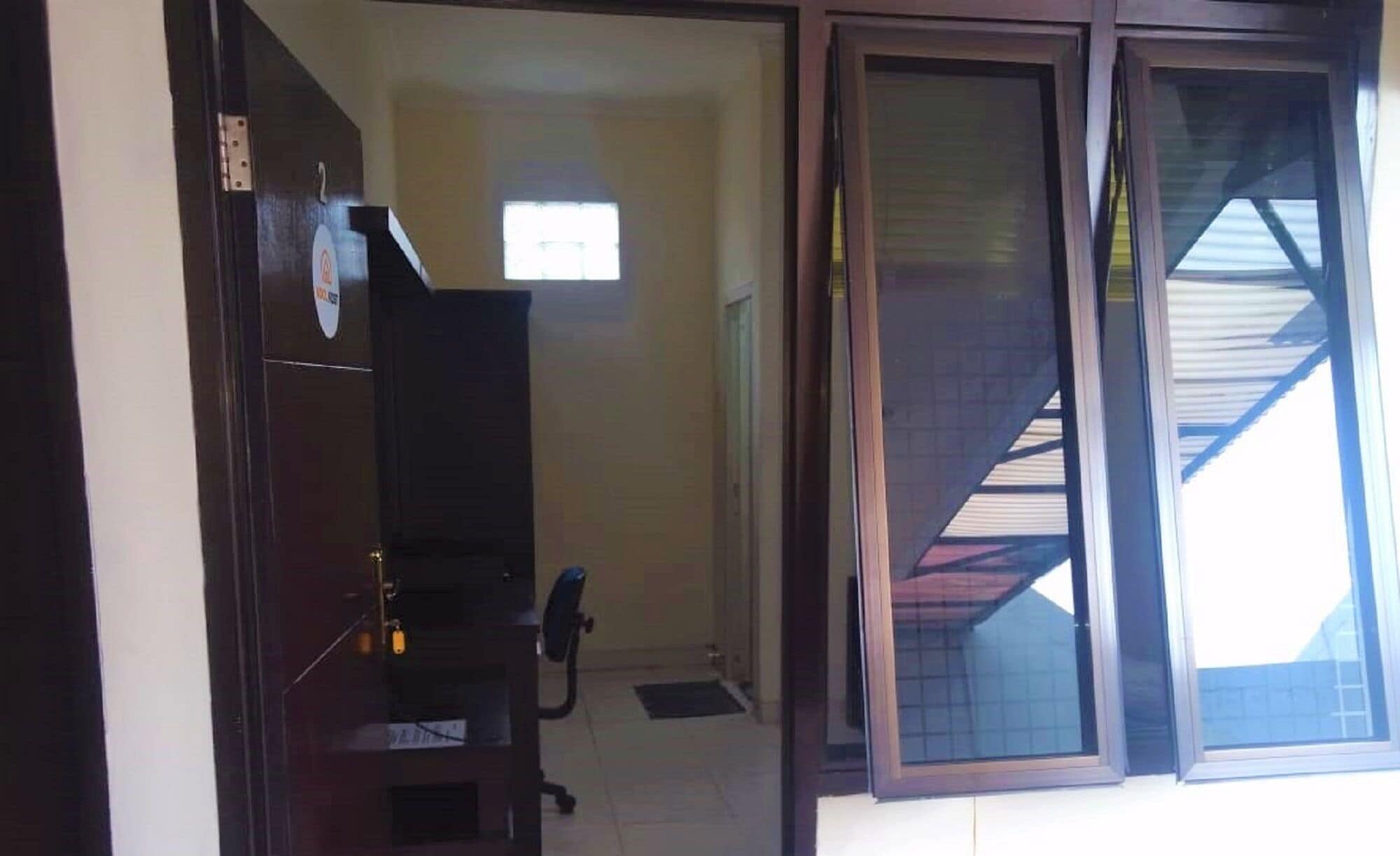 A room with a dark wooden wardrobe, a small window, and a door leading to another room.