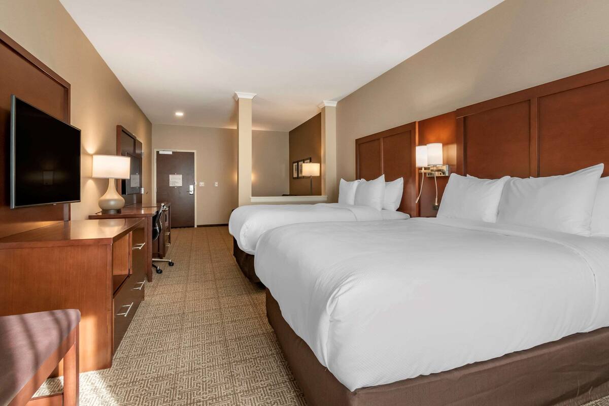 Quarto de hotel com uma cama grande, uma mesa com televisão de tela plana, uma luminária e um espelho.