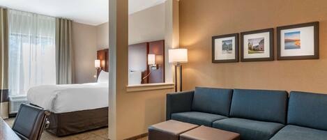 A hotel room with a bed, a sofa, a coffee table, a desk, and a chair. There are three framed pictures on the wall.