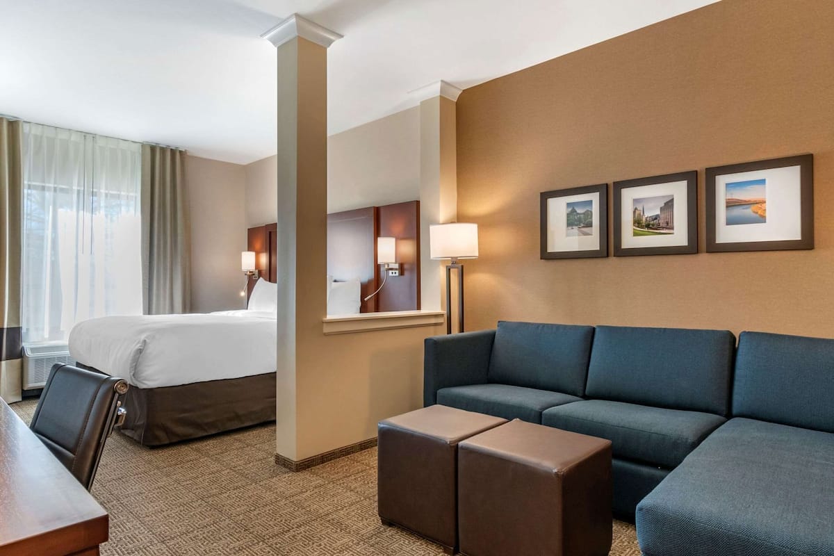 Quarto de hotel com cama, sofá, mesa de centro, escrivaninha e abajur.