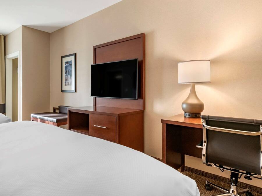 A hotel room with a large bed, a desk with a chair, a television, and a lamp.