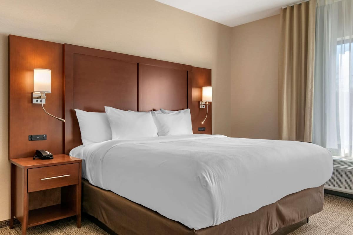Quarto de hotel com uma cama grande, duas mesas de cabeceira, um telefone e luminárias fixadas na parede.