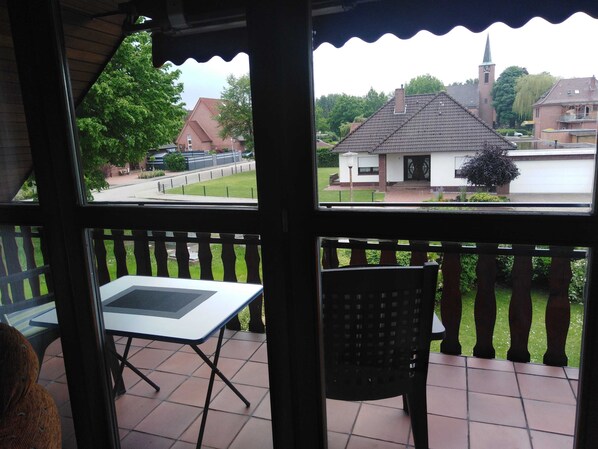 A balcony with a table and chair, overlooking a residential street with houses and a church.