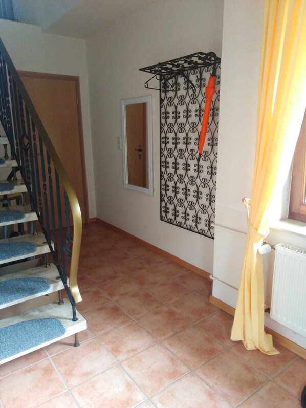 Uma escadaria com degraus forrados em carpete azul, um separador de metal decorativo e um radiador com cortina amarela.