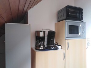 Uma cozinha compacta com micro-ondas, cafeteira e geladeira.