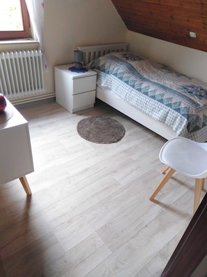 Um quarto com cama, mesa de cabeceira, escrivaninha e cadeira.