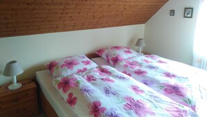 A bedroom with two beds, wooden headboard, a nightstand with a lamp, and a small wall decoration.