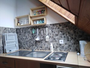 Uma cozinha com painel de pedra, prateleiras de madeira com temperos, uma pia, um fogão e utensílios pendurados.