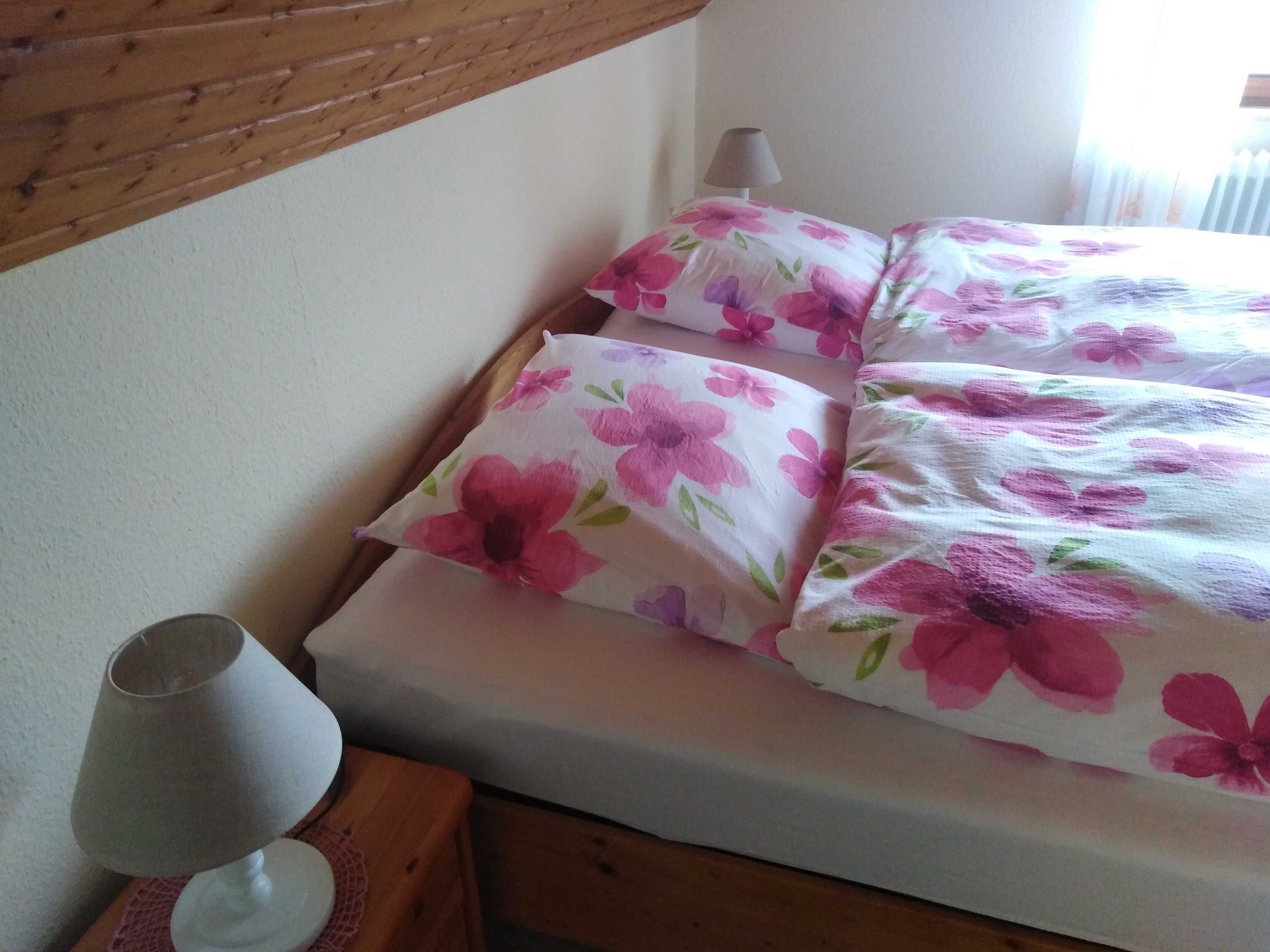 Una cama con ropa de cama floral, una lámpara de noche y un cabecero de madera.