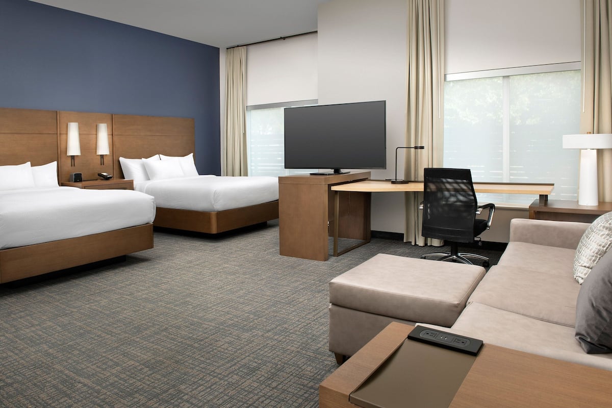 A hotel room with two beds, a desk, a television, a chair, and a sofa.
