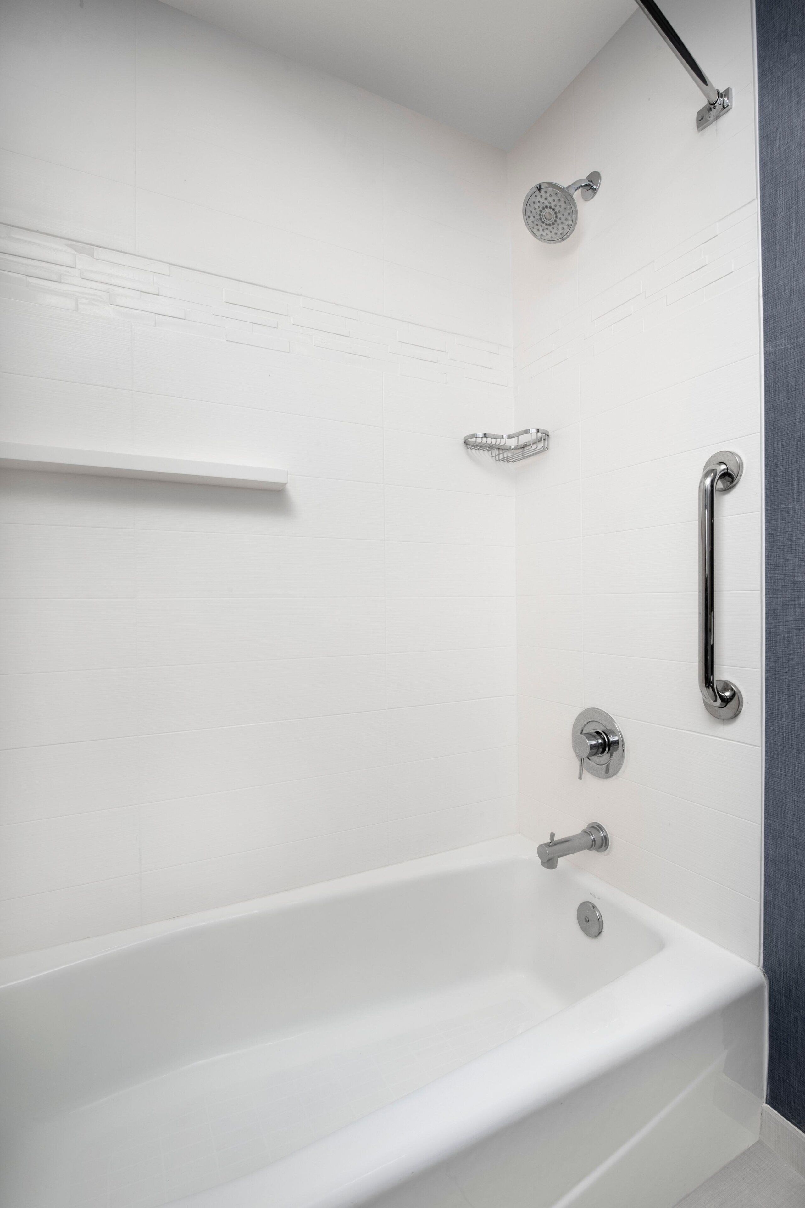A modern bathroom with a white bathtub, a showerhead, a handrail, and a towel rack.