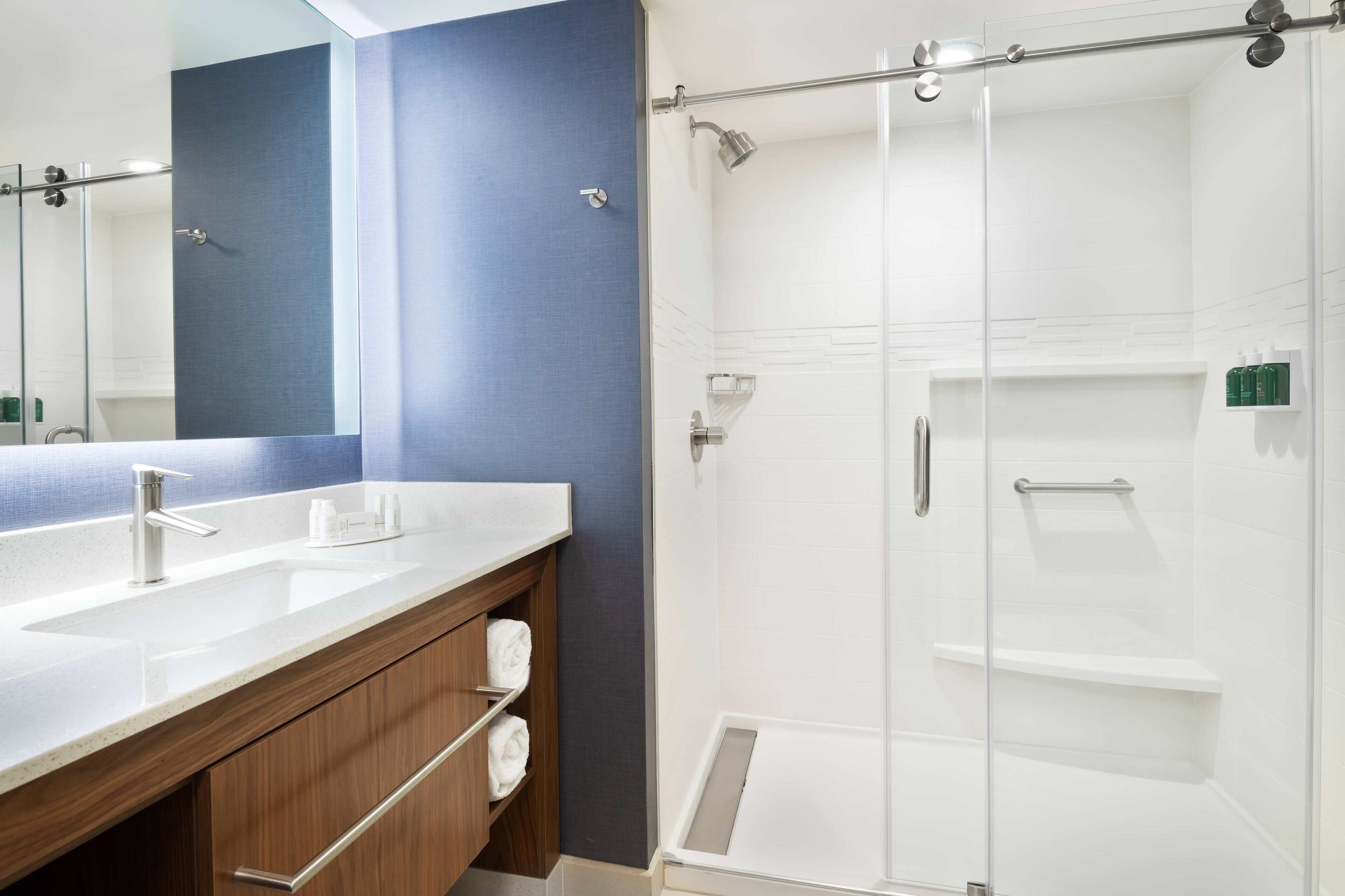 A modern bathroom with a large mirror, two sinks, a shower with a glass door, and a wooden vanity.