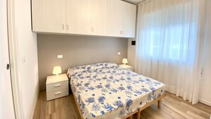 Une chambre à coucher comprenant un lit, deux tables de chevet, une commode, une armoire et une fenêtre avec des rideaux.