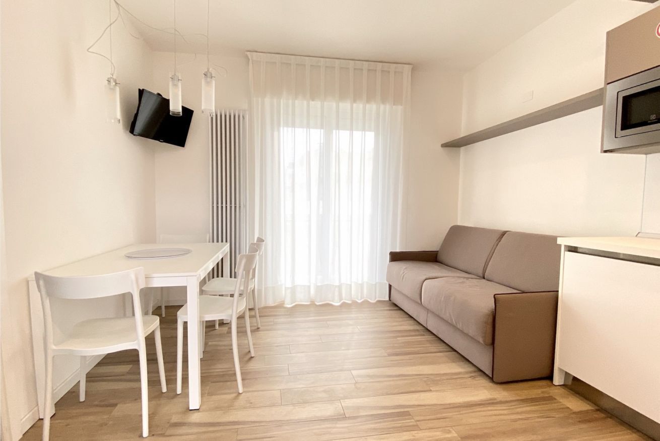 A modern, minimalist living space with a dining area, sofa, and a television mounted on the wall.