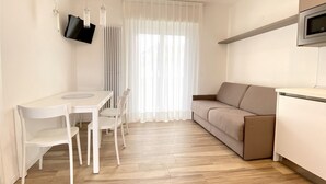 Un espacio habitable moderno y minimalista con comedor, sofá y televisor montado en la pared.