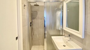 Une salle de bain moderne avec une douche à parois de verre, un lavabo blanc et un miroir au-dessus.