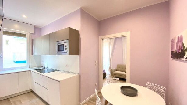 Une cuisine moderne avec des meubles blancs, un four à micro-ondes et un évier. On y trouve également un coin repas avec une table et des chaises blanches.