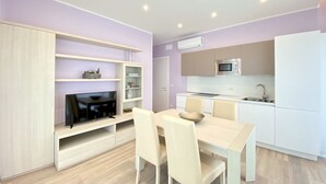 A modern kitchen with white cabinets, a microwave, and a dining area with a table and chairs. - Appartamento Palladio 2 - Carraro Immobiliare Jesolo (Lido di Jesolo)