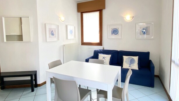 A dining area with a white table and chairs, a blue sofa, and framed pictures on the wall.
