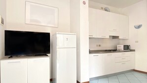 A compact kitchen with white cabinets, a built-in microwave, and a flat-screen TV.