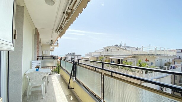 Ein Balkon mit weißem Stuhl und Tisch, einem Metallgeländer und Blick auf Gebäude im Hintergrund.