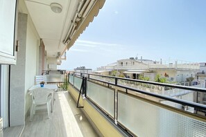 Un balcon avec une chaise et une table blanches, une rambarde en métal et une vue sur des bâtiments en arrière-plan.