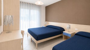 Une chambre d’hôtel avec deux lits, un bureau, une chaise, une table de chevet et une fenêtre avec des rideaux.