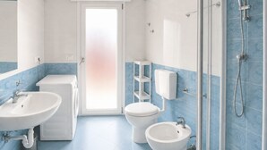 Une salle de bain avec deux lavabos, des toilettes, une douche et une porte donnant sur une autre pièce.