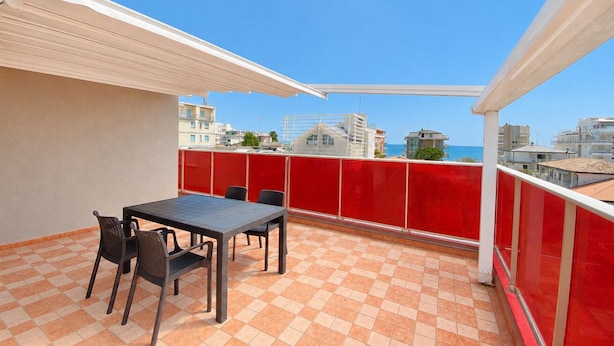 Un balcón con piso a cuadros, una mesa con sillas y barandilla roja.