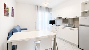 Eine moderne Küche mit weißen Schränken, einem Esstisch mit Stühlen, einem blauen Sofa und einem Fernseher.